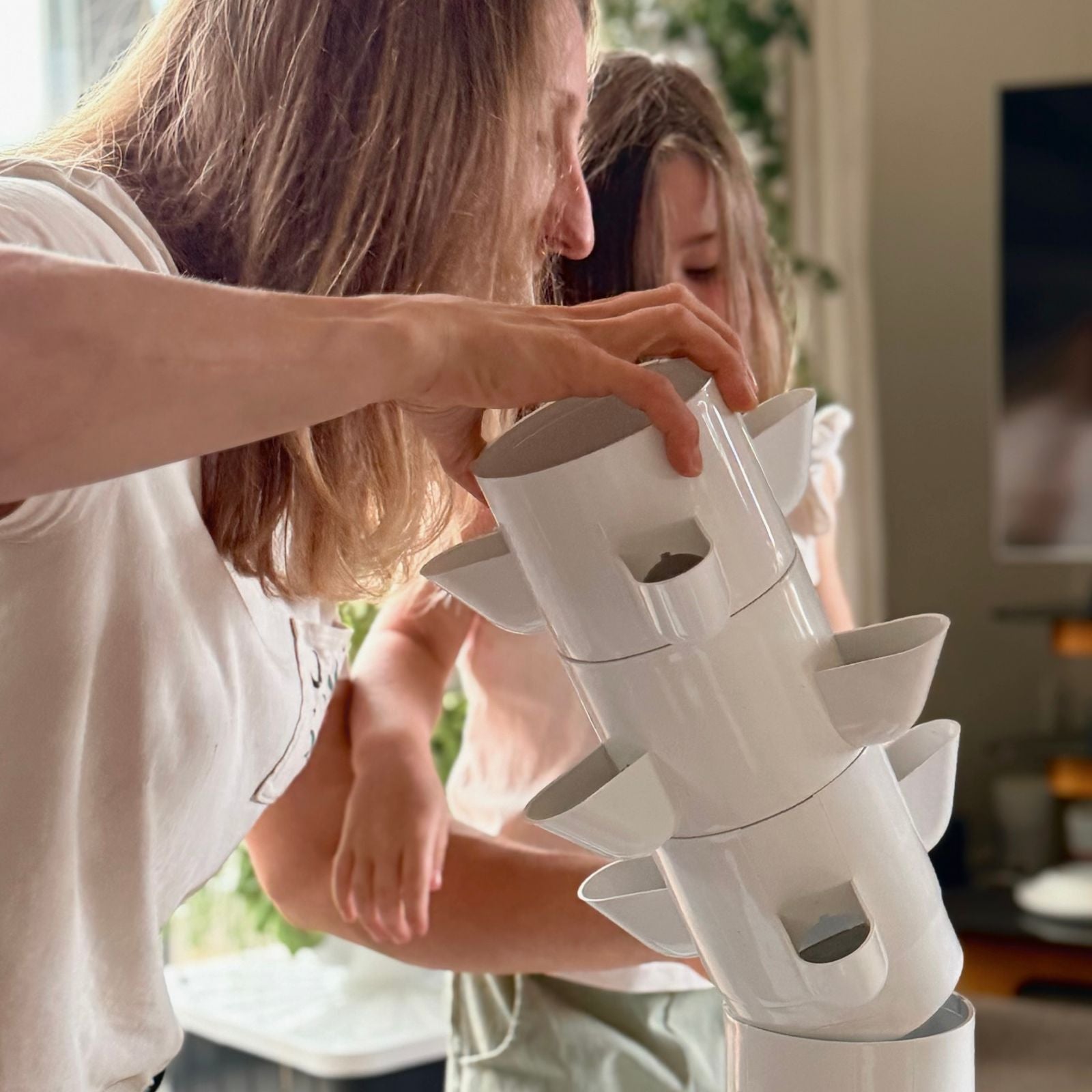 Two people interacting with a white indoor plant grow system in a home setting.